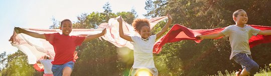 Drei Kinder laufen mit wehenden Tüchern über dem Kopf über eine Wiese. Es steht "Noch Plätze frei" im Bild. 
