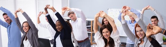 Elf Menschen machen Dehnübungen im Büro. Sie haben die Arme über dem Kopf. Es steht "Noch Plätze frei" im Bild. 