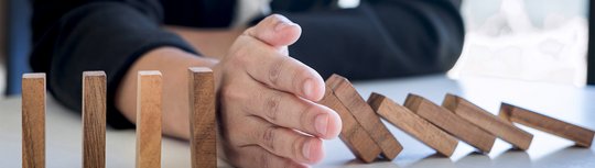 Ein Mensch steckt seinen Arm ziwschen eine Reihe umfallender Dominosteine um die Kette zu stoppen. Im Bild steht "Noch Plätze frei". 